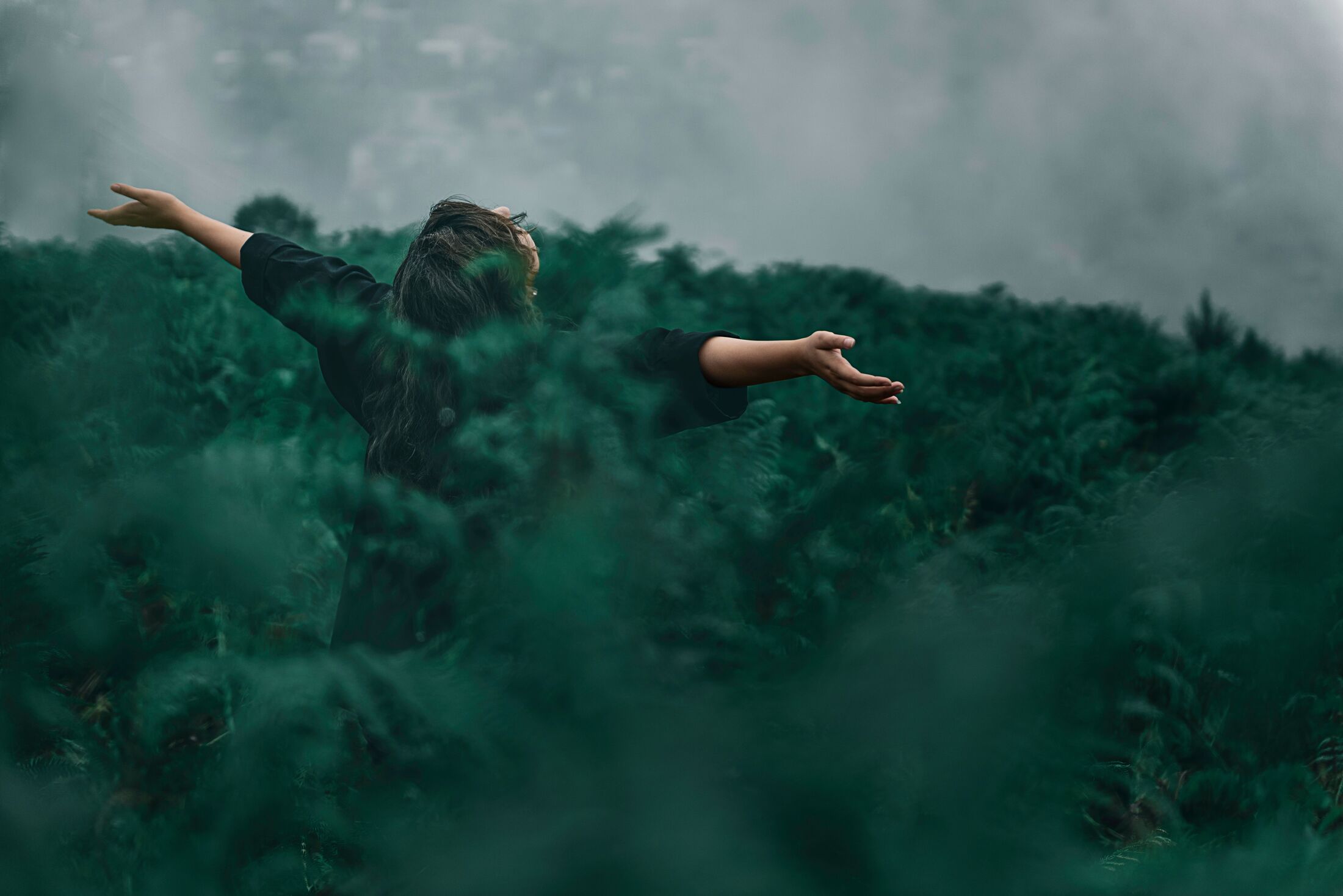 Vrouw met wijd gespreide armen in een groen landschap
